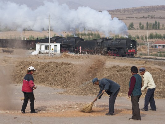 Eastbound Jitong Railway freight train passing farmers winnowing wheat by hand near Xigou, Inner Mongolia, during the 2005 harvest.