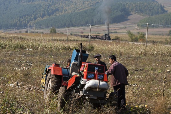 Farmers in the valley east of Tuoyaozi use a tractor to harvest pumpkin seeds as an empty coal train passes in the background on the narrow-gauge Huanan Forestry Railway. September 27, 2005.