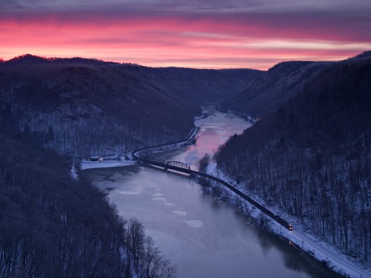 At the peak of a winter sunrise, a CSX westbound empty coal train crosses the icy New River at Hawks Nest, West Virginia.