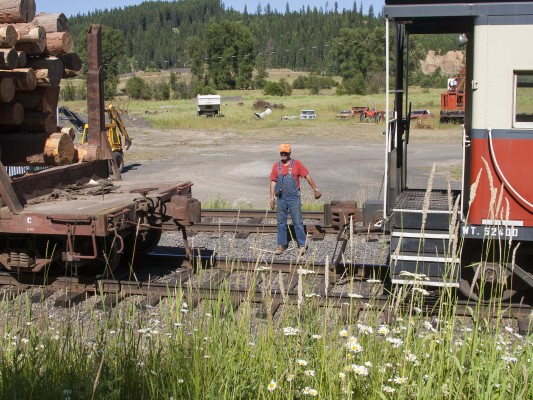 St. Maries River Railroad conductor Pat Hough guides the coupling of his caboose to the outbound Clarkia Logger. The train has just swapped its empty log cars for loads at the reload facility in Clarkia, Idaho, and is preparing to make the return trip to St. Maries on a bright July afternoon in 2005.