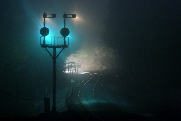 Former Baltimore & Ohio position light signals glow green through the fog as a westbound CSX freight train approaches Carothers Tunnel on the Magnolia Cutoff near Paw Paw, West Virginia.