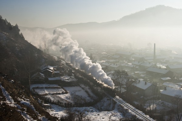 A narrow-gauge 0-8-0 C2 locomotive steams through the village of Tuoyaozi, Heilongjiang, China, with an eight-car loaded coal train on the hazy morning of December 1, 2005.